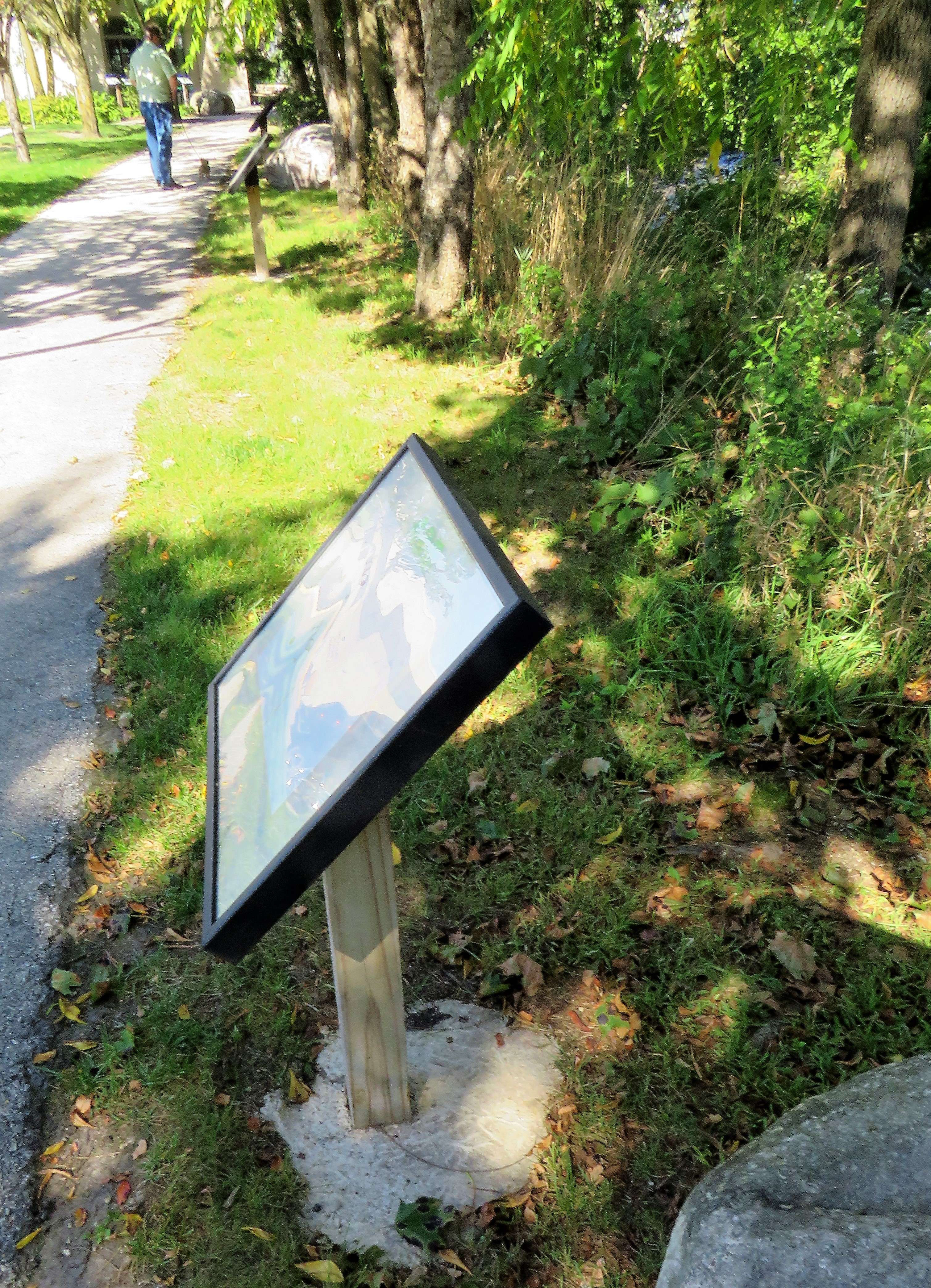 A close-up of an angled StoryWalk reader frame on a wooden post